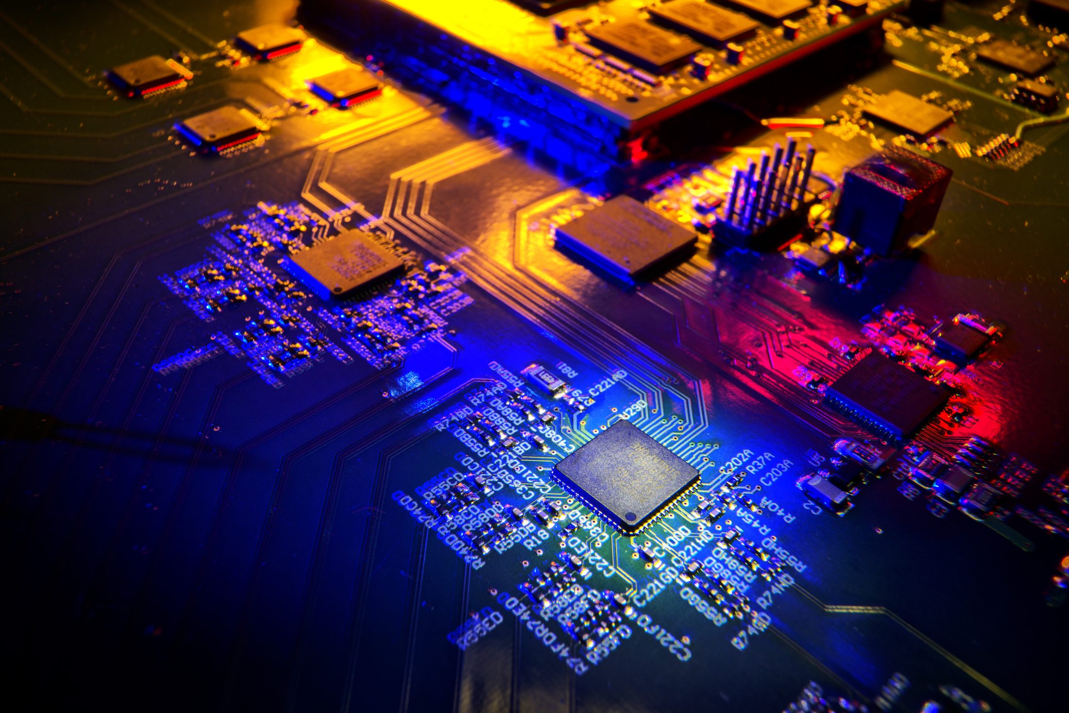 Renkli aydınlatma altında elektronik kartın yakın planı; devre yolları ve entegre bileşenler